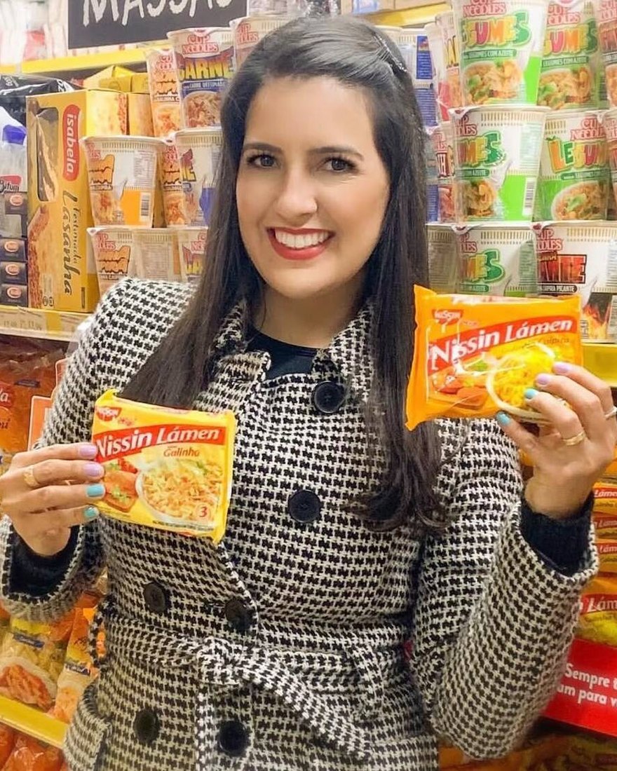 Dani Moy no corredor de massas do supermercado, segurando dois produtos